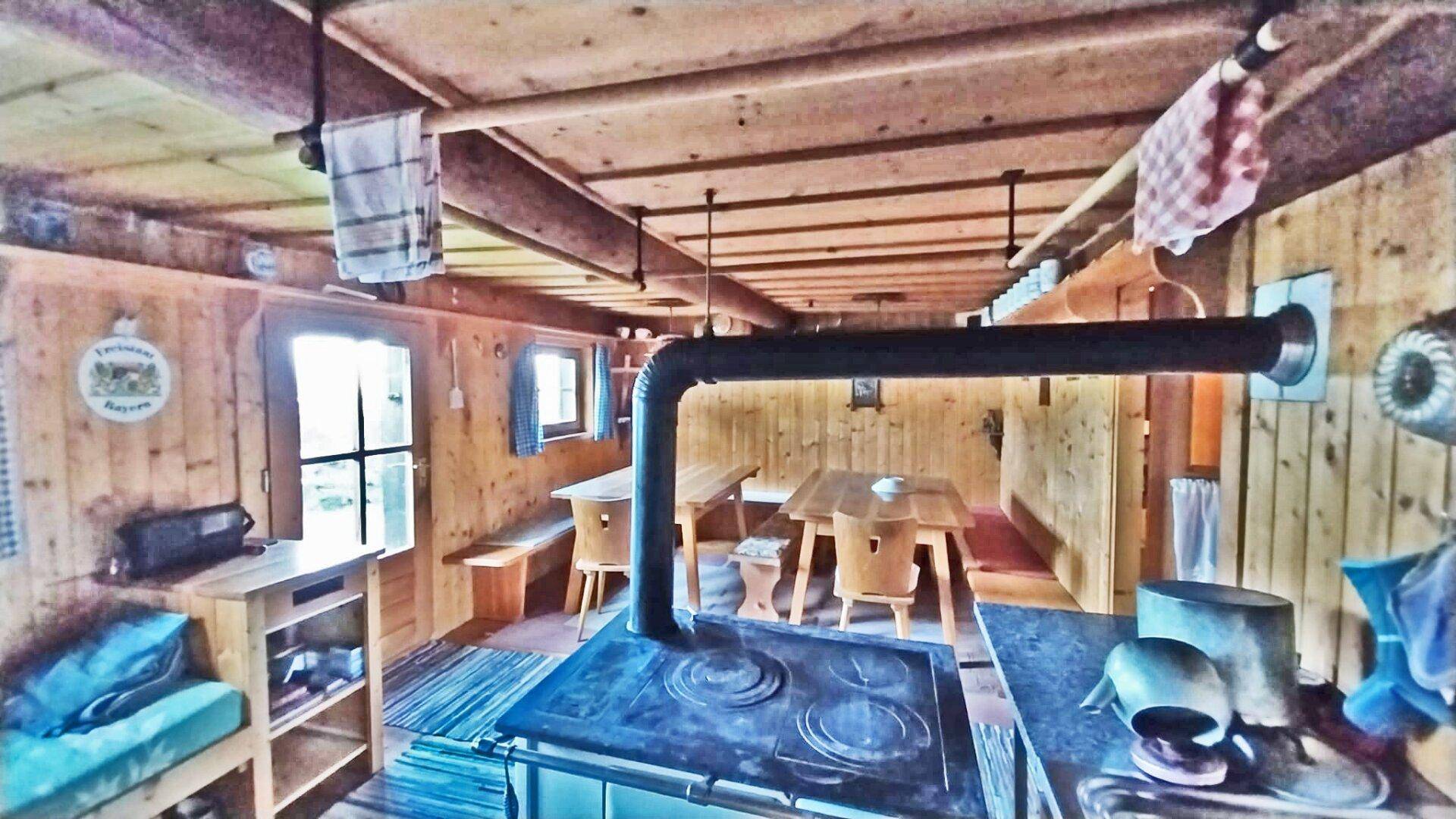 Gemütlicher Wohn- und Essbereich in einer Holzhütte mit traditionellem Holzofen und Holztischen.
