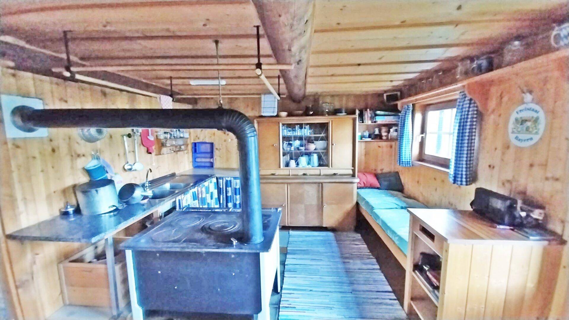 Rustikale Wohnküche mit Holzofen, einfacher Küchenzeile und einer gemütlichen Schlafbank.