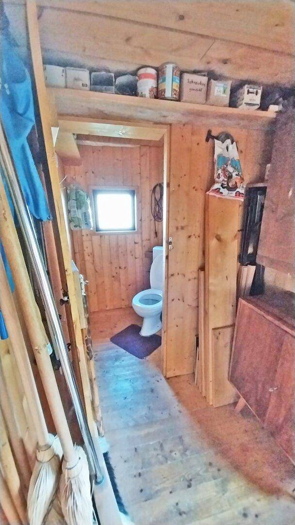 Einfaches WC mit Holzwänden und einem kleinen Fenster, typisch für eine Berghütte.