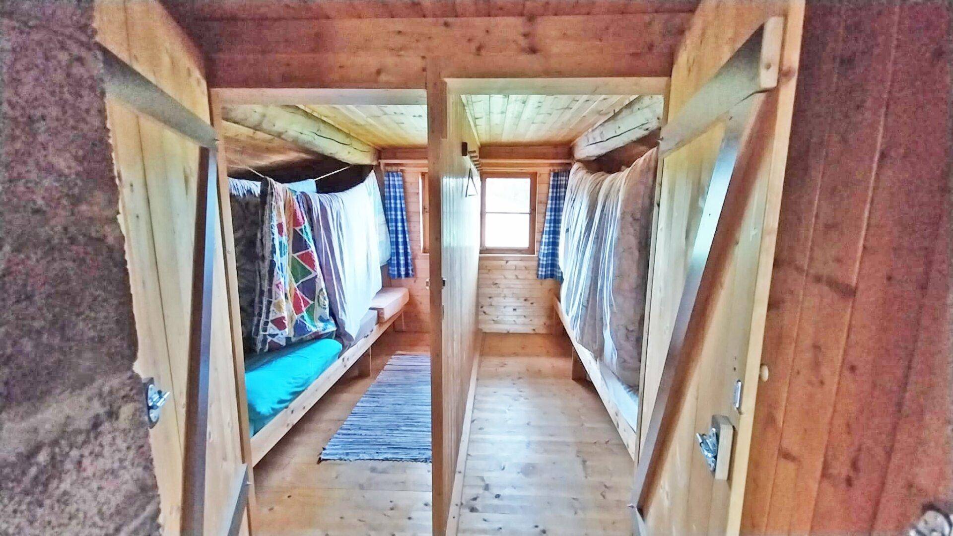 Rustikales Schlafzimmer in einer Holzhütte mit mehreren Betten und einfacher Einrichtung.