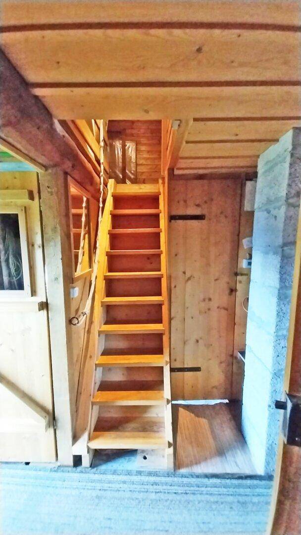 Rustikale Holztreppe, die zu einem oberen Bereich der Hütte führt, umgeben von Holzwänden.