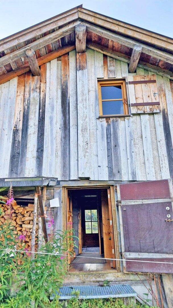 Traditionelle Holzhütte mit verwitterter Fassade, Holzlager und Blick auf die Natur.