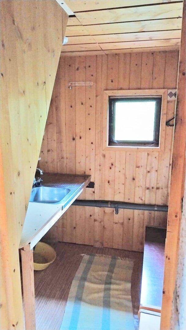 Kleine, einfache Küchenzeile in einer Holzhütte mit Spülbecken und Holzvertäfelung.