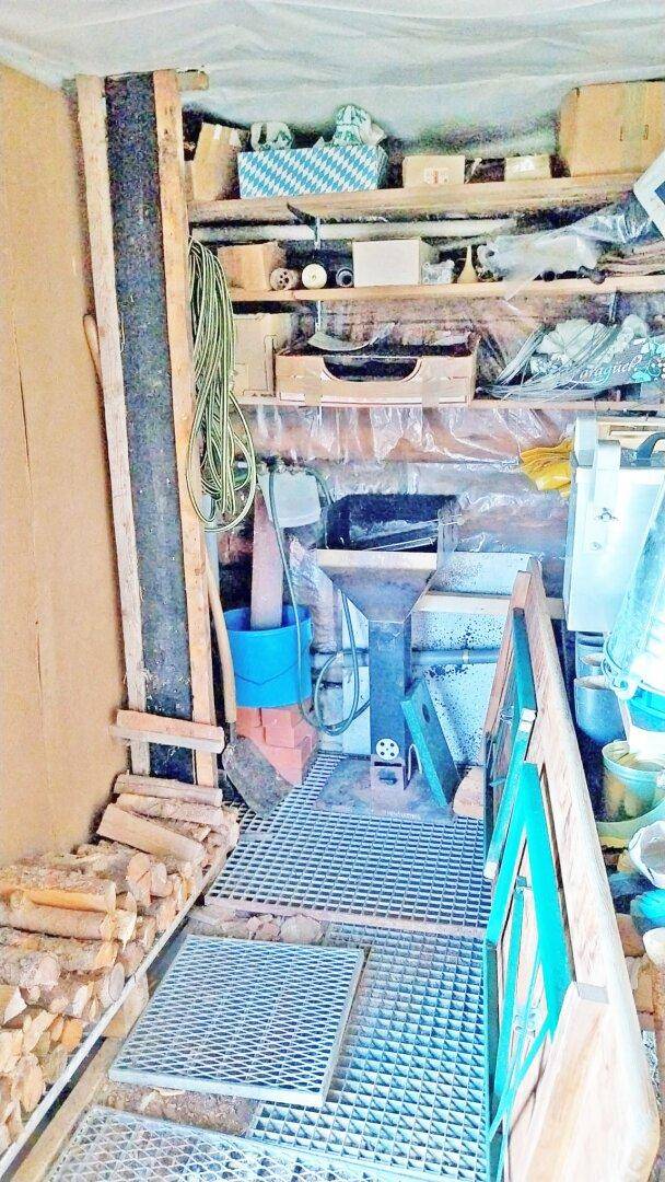 Rustikaler Abstellraum mit Holzstapeln, Metallrosten und verschiedenen Utensilien.