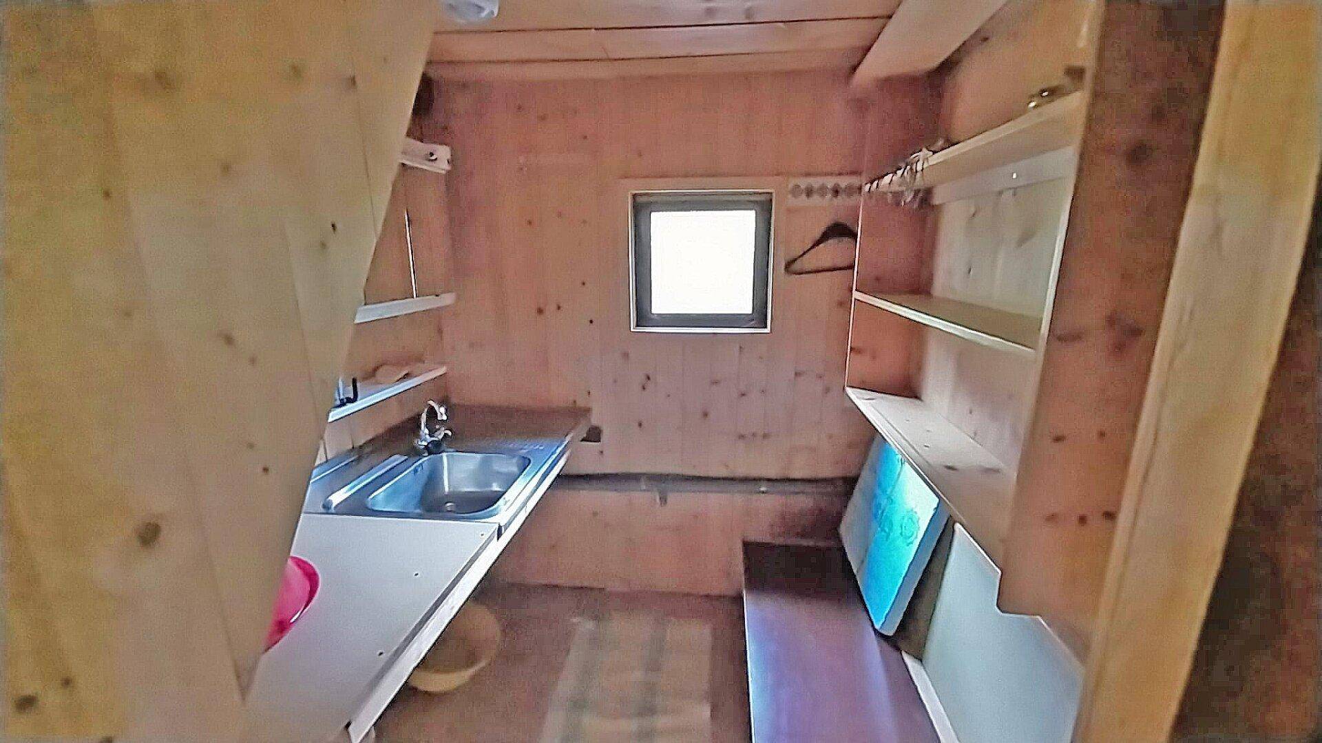 Einfache Küchenzeile in einer Holzhütte mit Spülbecken, Regalen und kleinem Fenster.