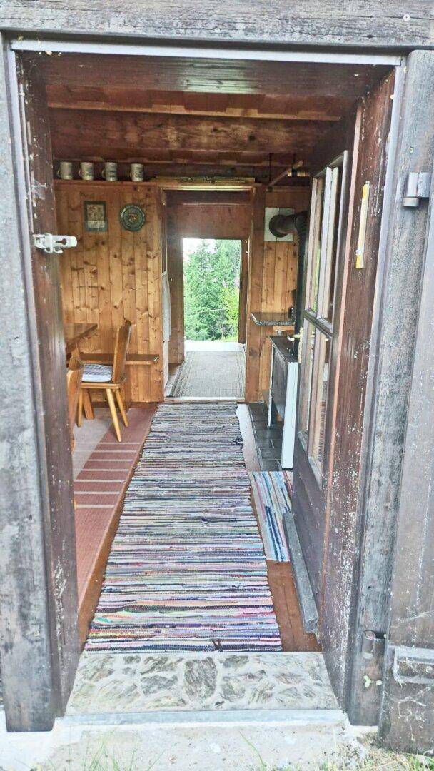 Eingangsbereich der Hütte mit Holzboden und -wänden, der in den Wohnbereich führt.