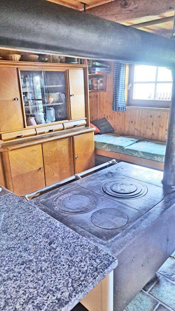 Traditionelle Küche mit Holzofen, Anrichte und Sitzbank am Fenster in einer Hütte.