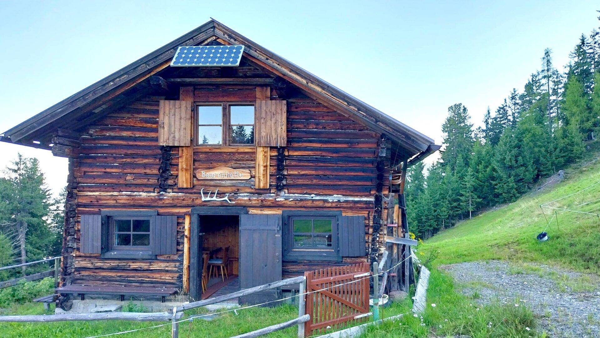 Traditionelle Holzhütte mit Solarpaneel auf dem Dach und rustikalen Holzfensterläden in alpiner Umgebung.