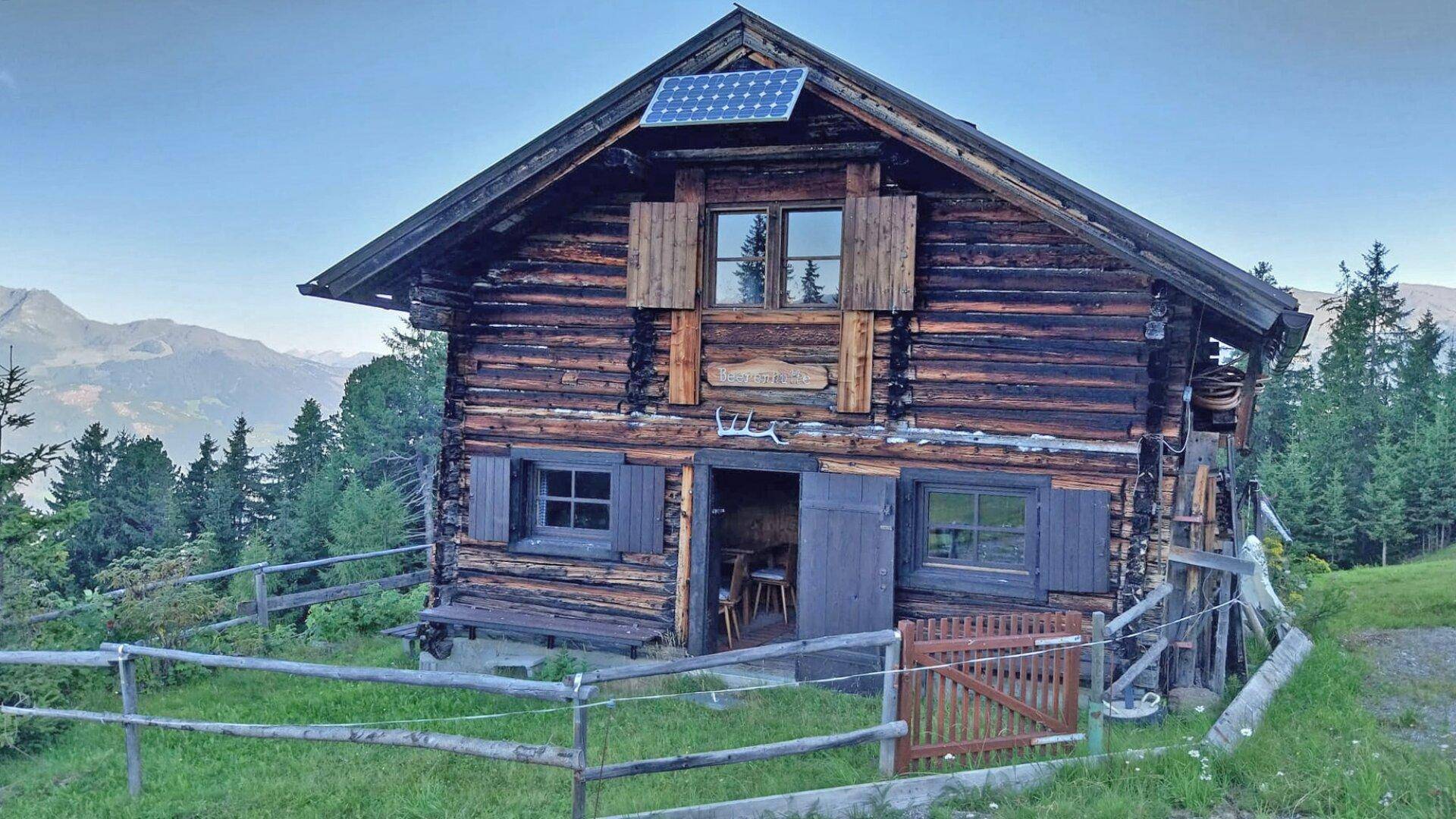 Rustikale Holzhütte in den Bergen mit Solarpaneel auf dem Dach und traditionellen Fensterläden.