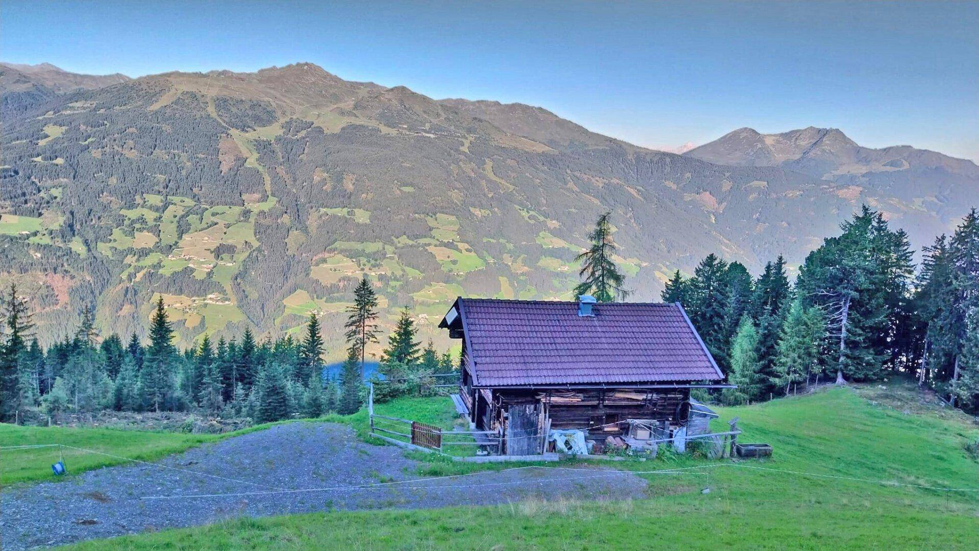 Gemütliche Holzhütte in den Alpen, eingebettet in eine grüne Landschaft mit majestätischen Bergen.