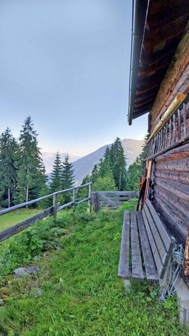Rustikale Holzbank neben der Hütte mit weitem Blick auf die umliegenden Berge und Wälder.
