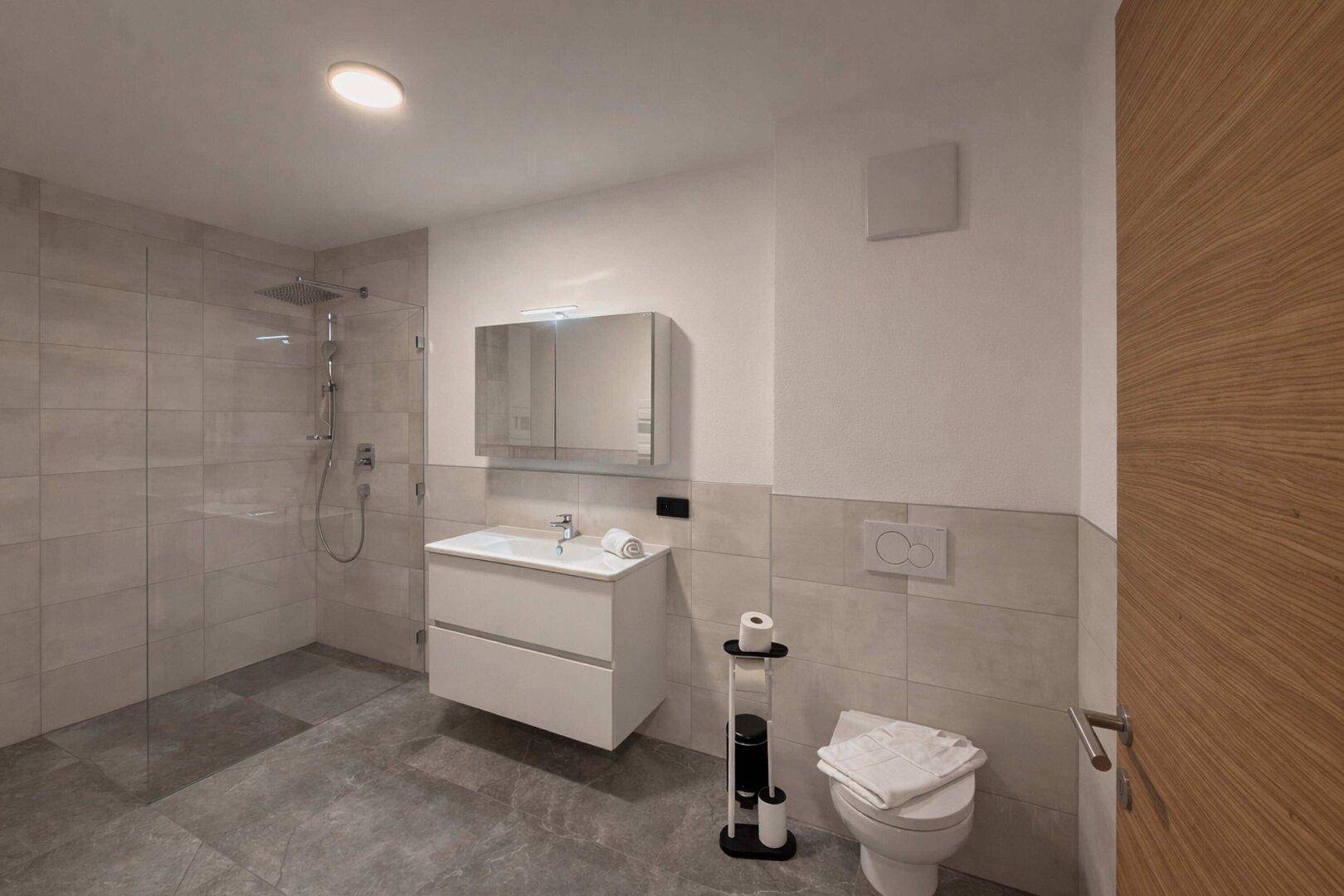 Modernes Badezimmer mit Dusche, Toilette, Waschtisch und Spiegelschrank.