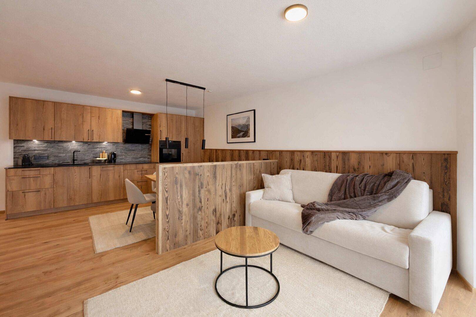 Heller Wohnbereich mit Holzboden, offener Küche und modernem Sofa.