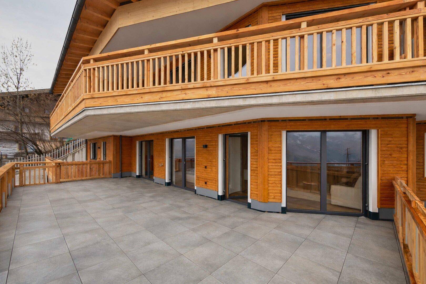 Große geflieste Terrasse mit Holzgeländer und Blick auf die umliegende Landschaft.