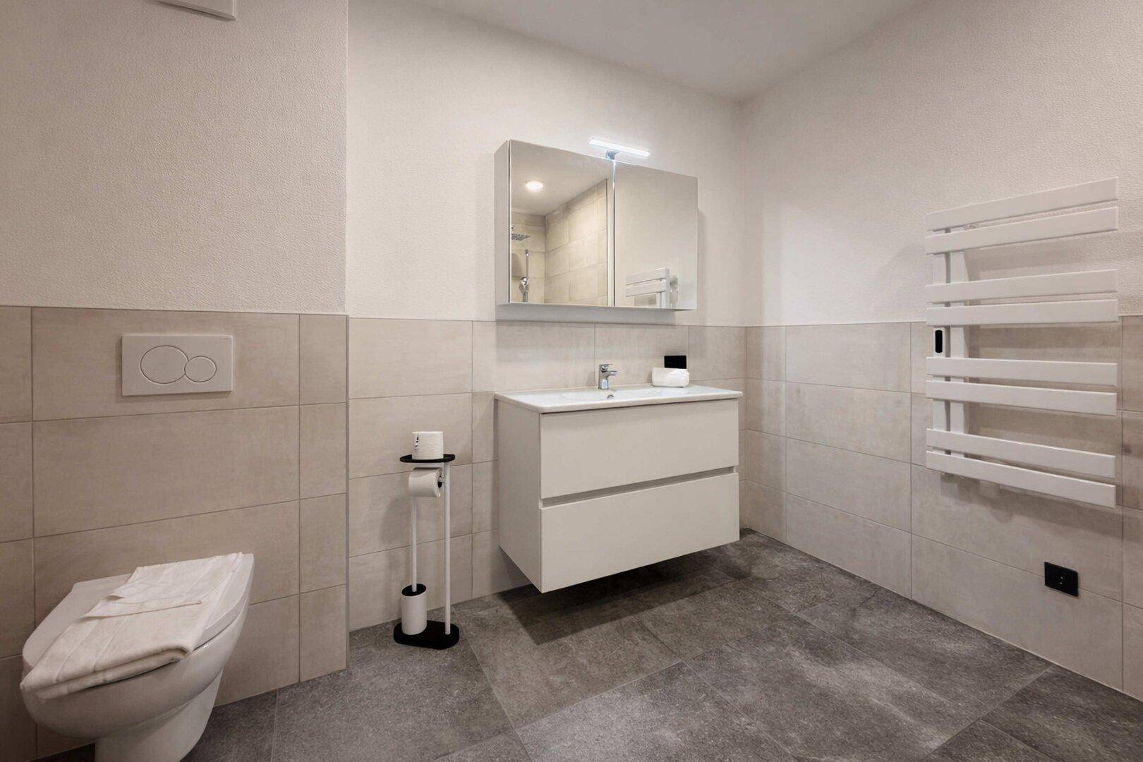 Modernes Badezimmer mit Dusche, Toilette, Waschtisch und beheiztem Handtuchhalter.
