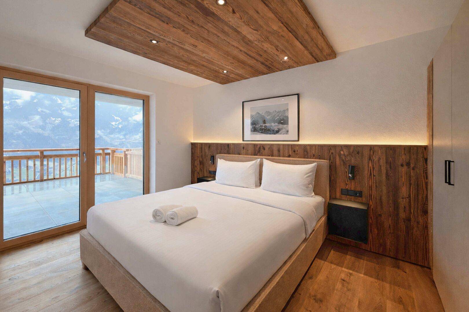 Schlafzimmer mit Holzboden, Holzakzenten und Zugang zu einem Balkon mit Bergblick.