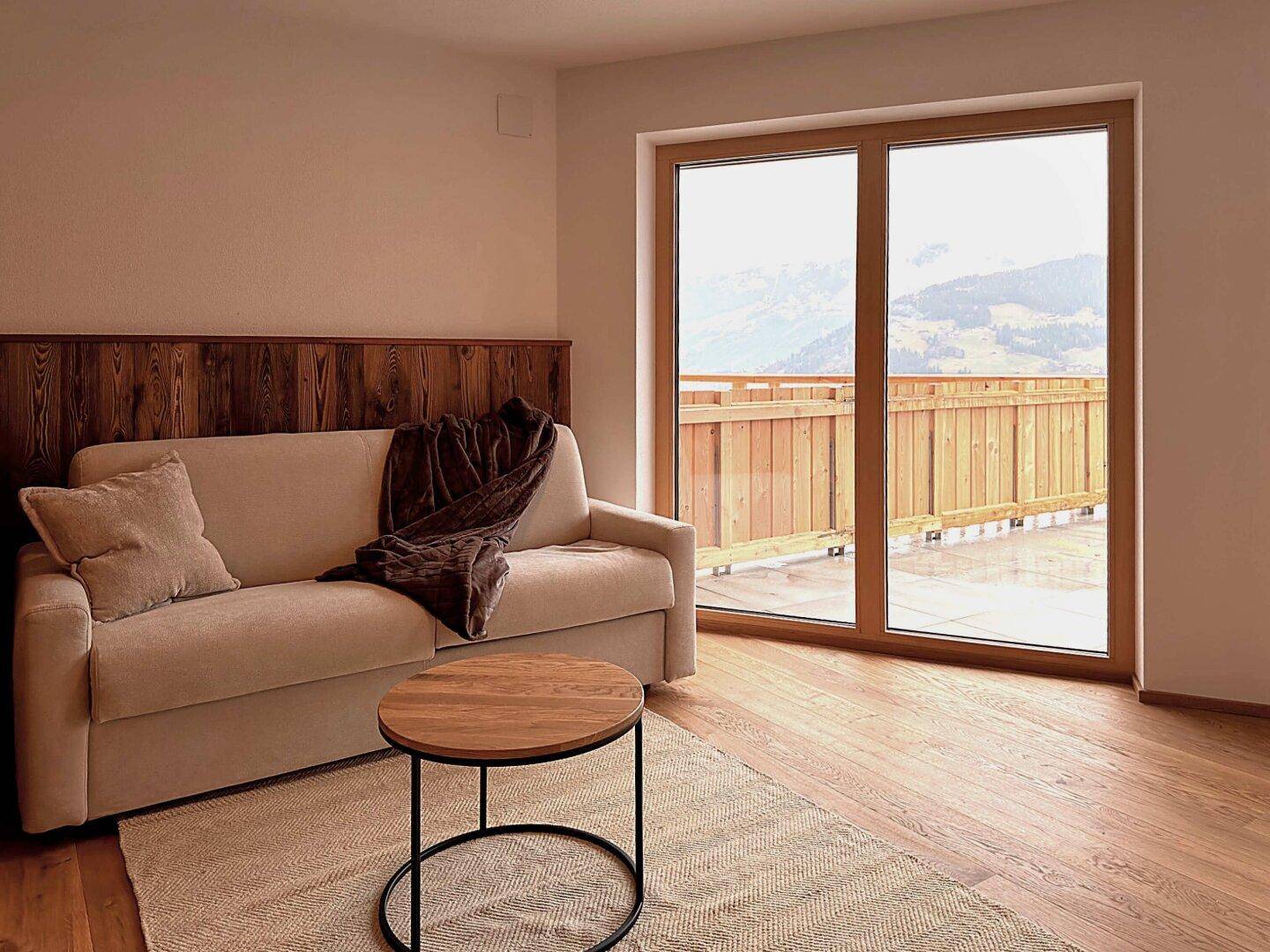 Heller Wohnbereich mit Sofa, Holzboden und Zugang zu einem Balkon mit Bergblick.
