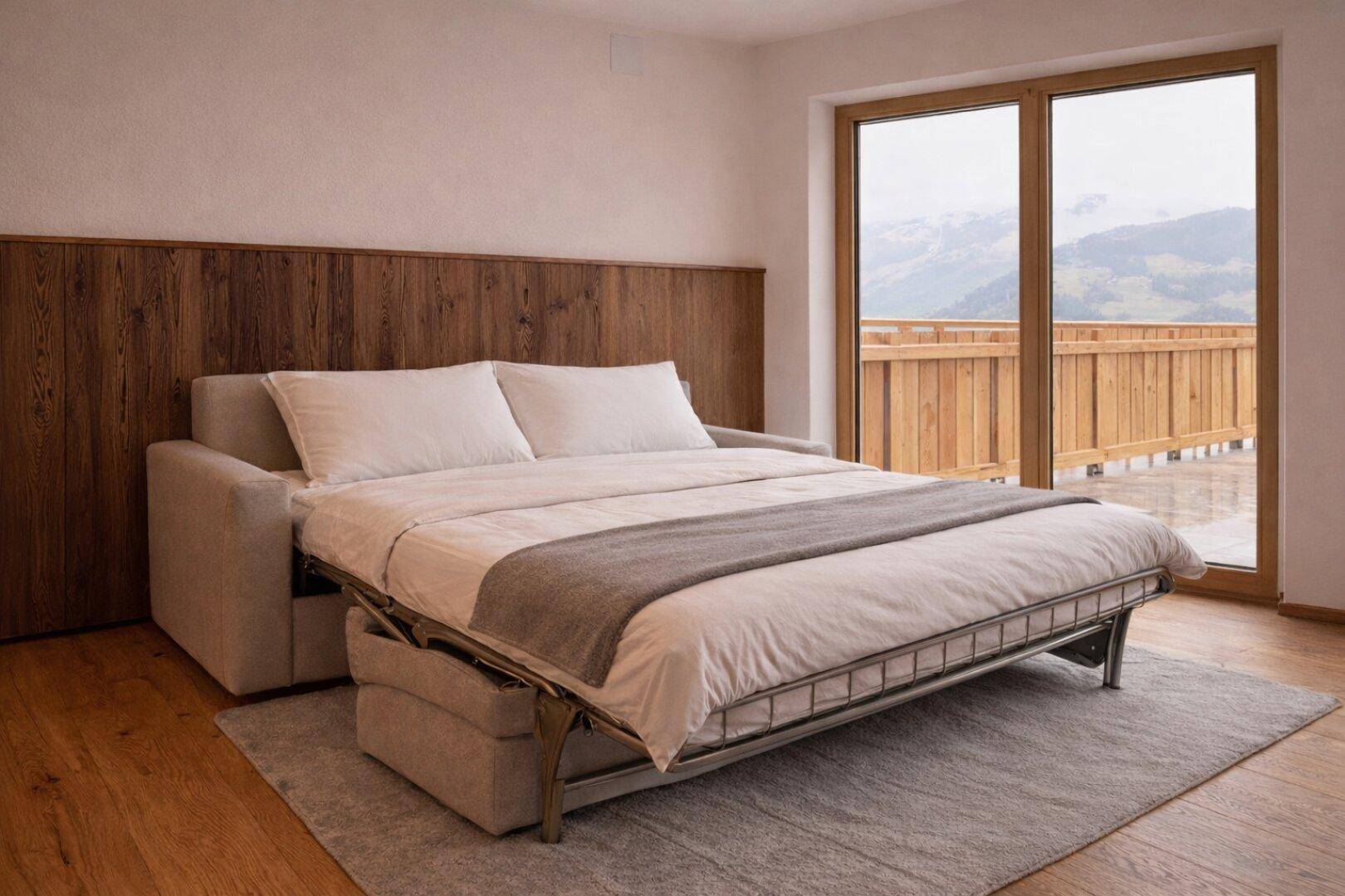 Wohnbereich mit ausziehbarem Schlafsofa, Holzboden und Zugang zu einem Balkon mit Bergblick.