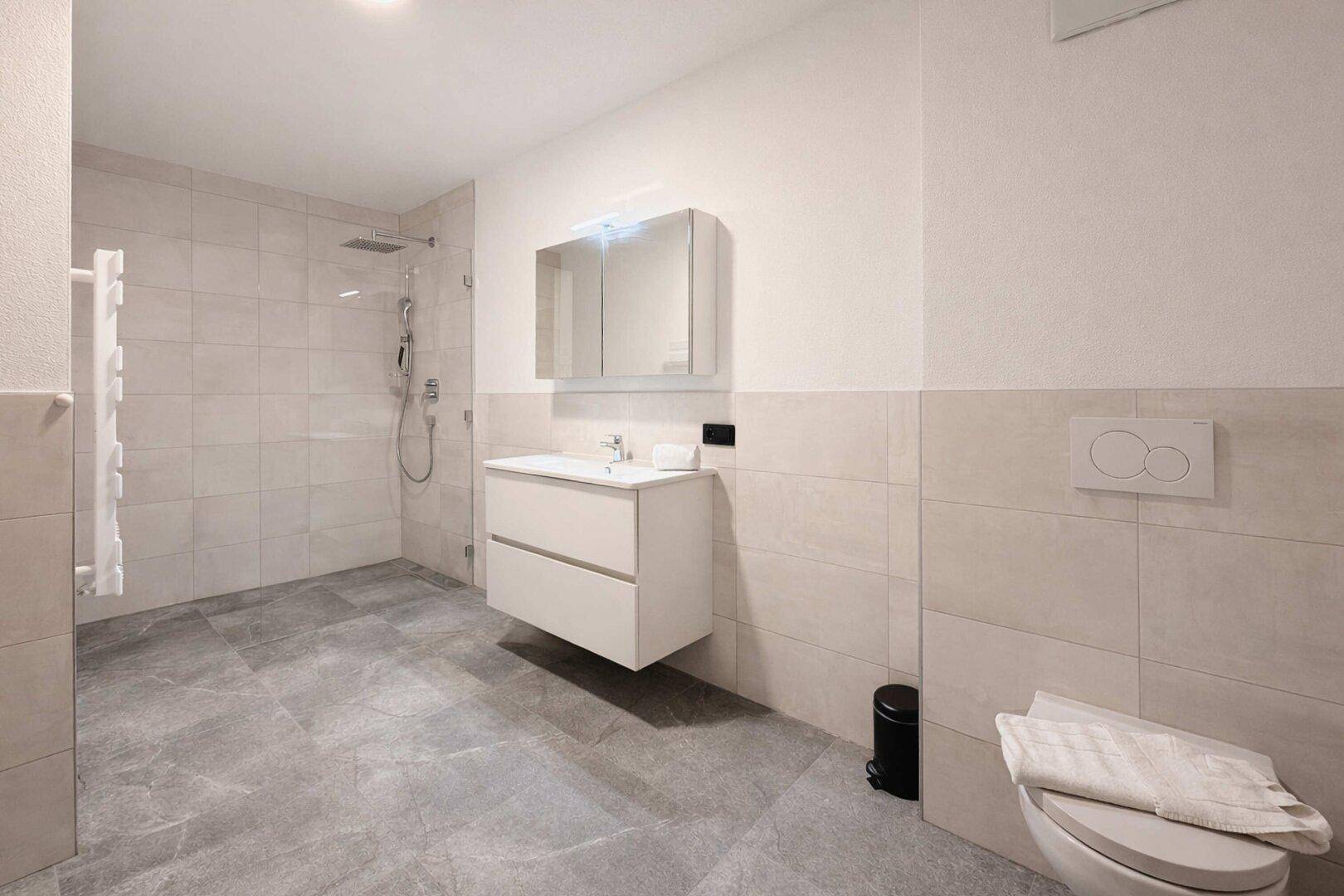 Helles, modernes Badezimmer mit ebenerdiger Dusche, WC und Waschbecken.