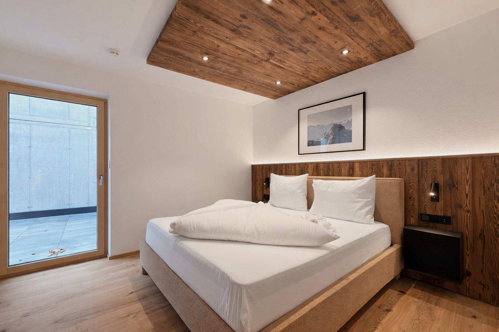 Helles Schlafzimmer mit Doppelbett, Holzboden und direktem Zugang zu einem Außenbereich.