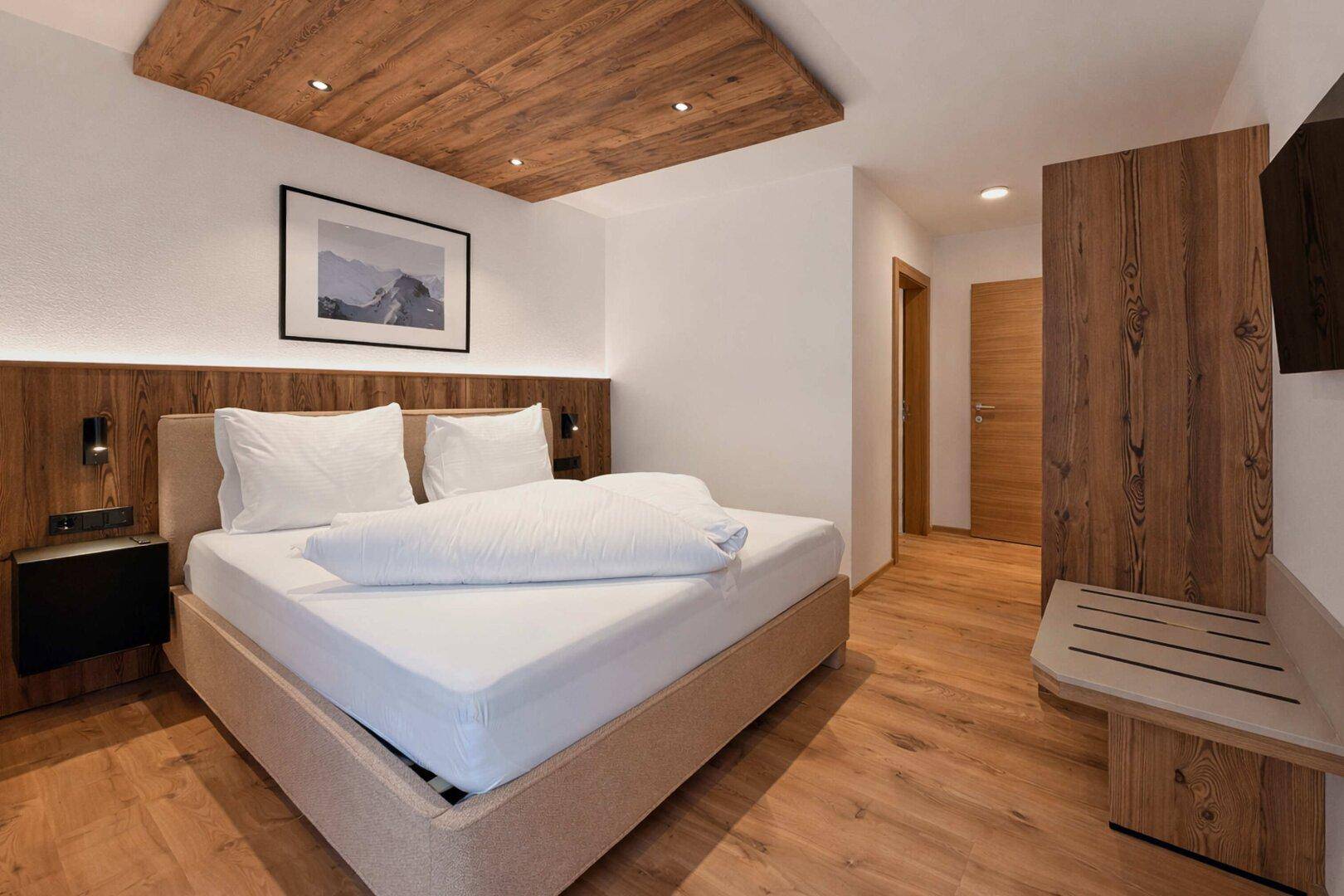 Modernes Schlafzimmer mit Holzboden, Holzbett und einem an der Wand montierten Fernseher.