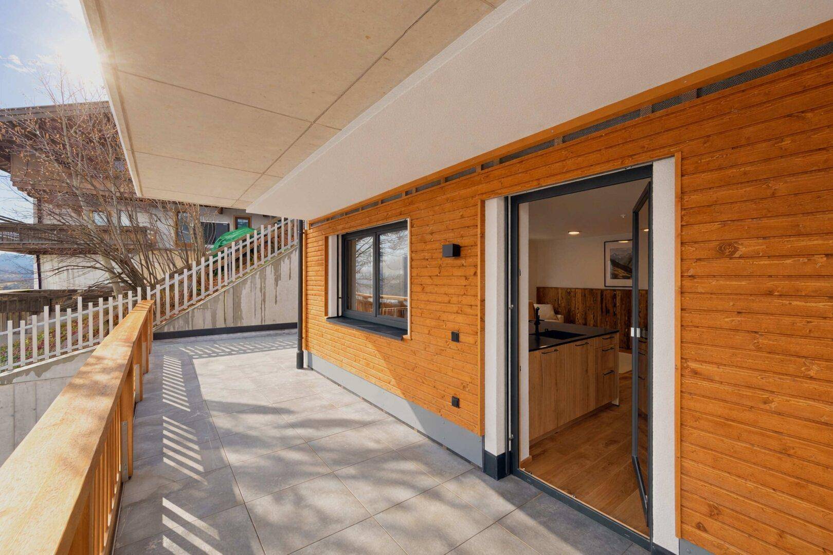 Große geflieste Terrasse mit Holzwandverkleidung und Zugang zum Innenbereich der Wohnung.