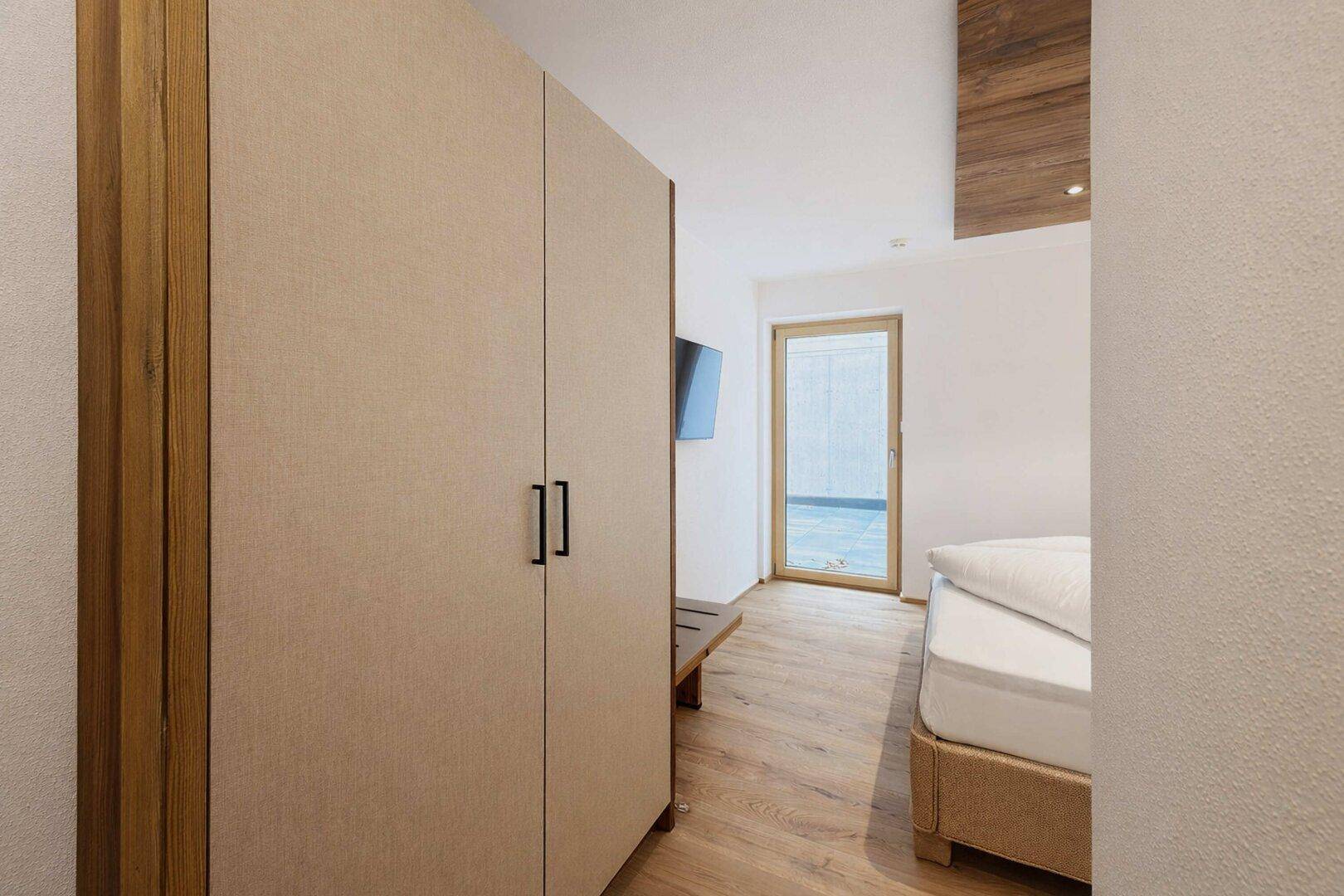 Schlafzimmer mit hellem Einbauschrank, Holzboden und Zugang zu einem Außenbereich.