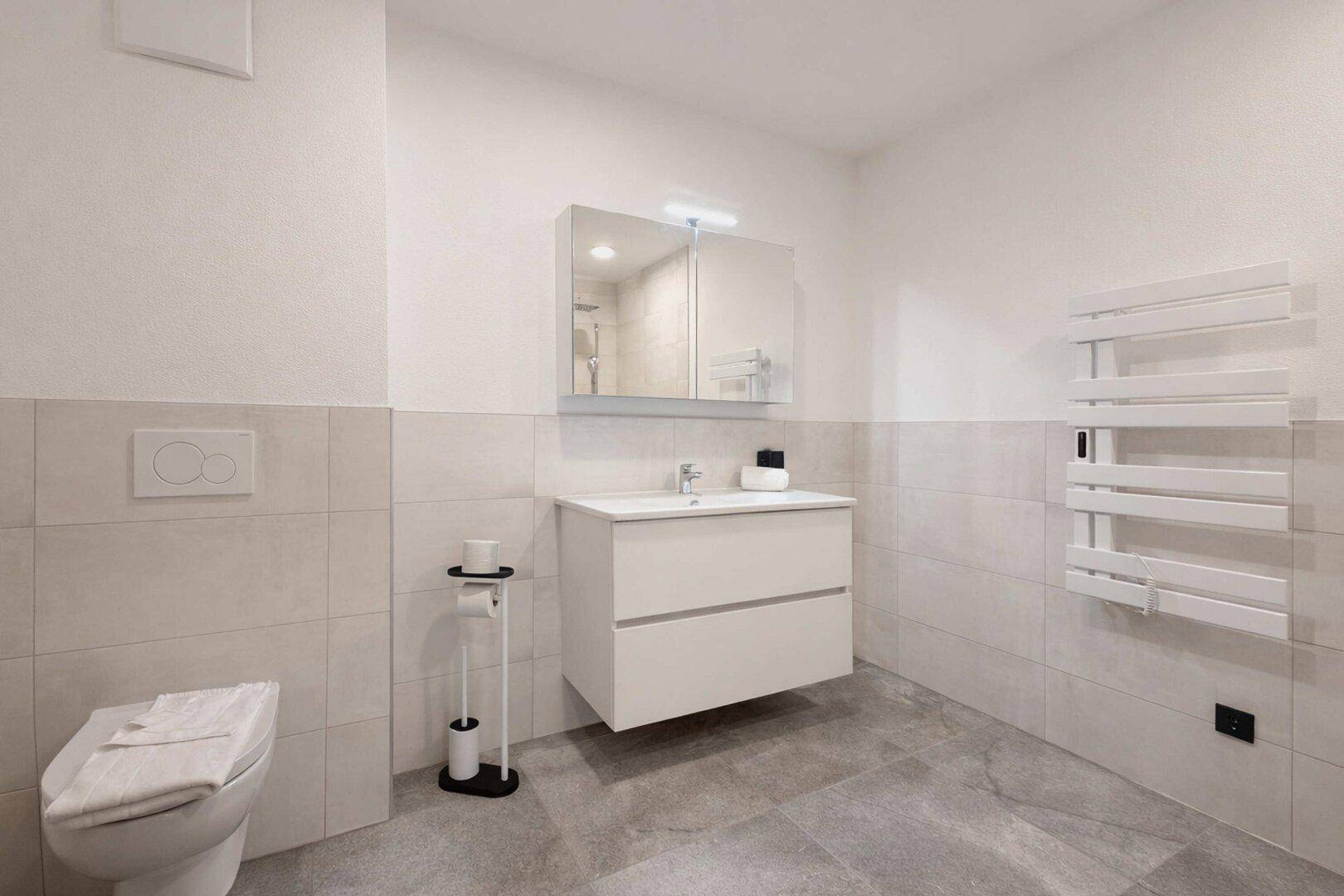 Modernes Badezimmer mit WC, Waschbeckenunterschrank und beheiztem Handtuchhalter.