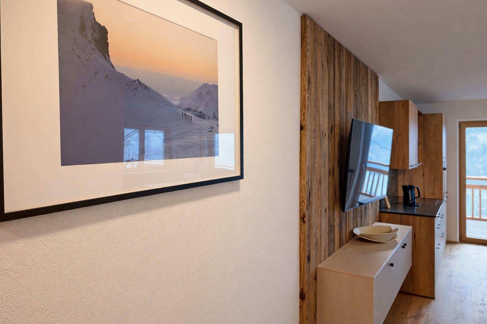 Wandbereich im Wohnzimmer mit Fernseher, Kunstwerk und Blick auf die Berge.