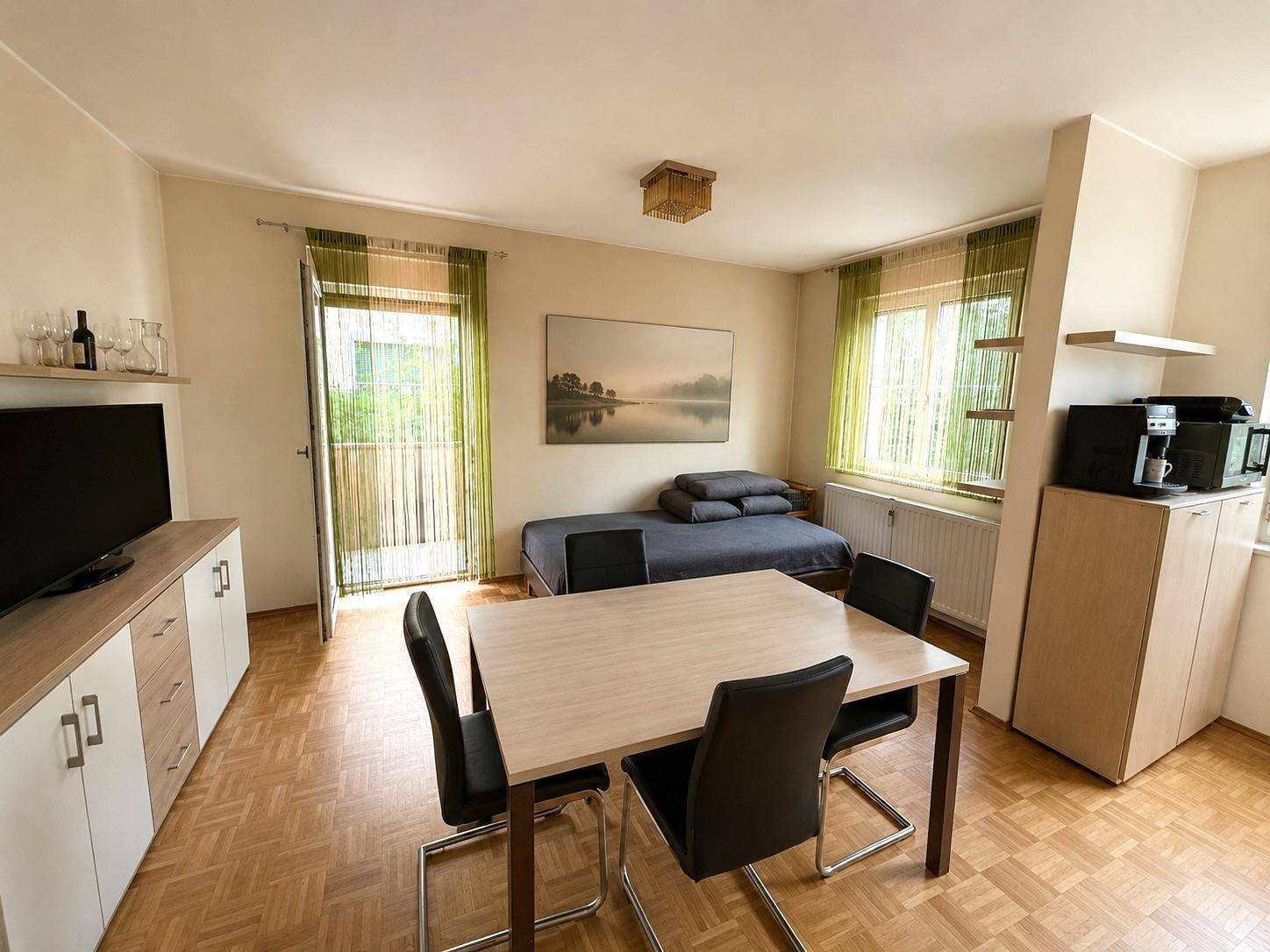 Heller Wohnbereich mit Esstisch, Schlafsofa und Zugang zum Balkon.