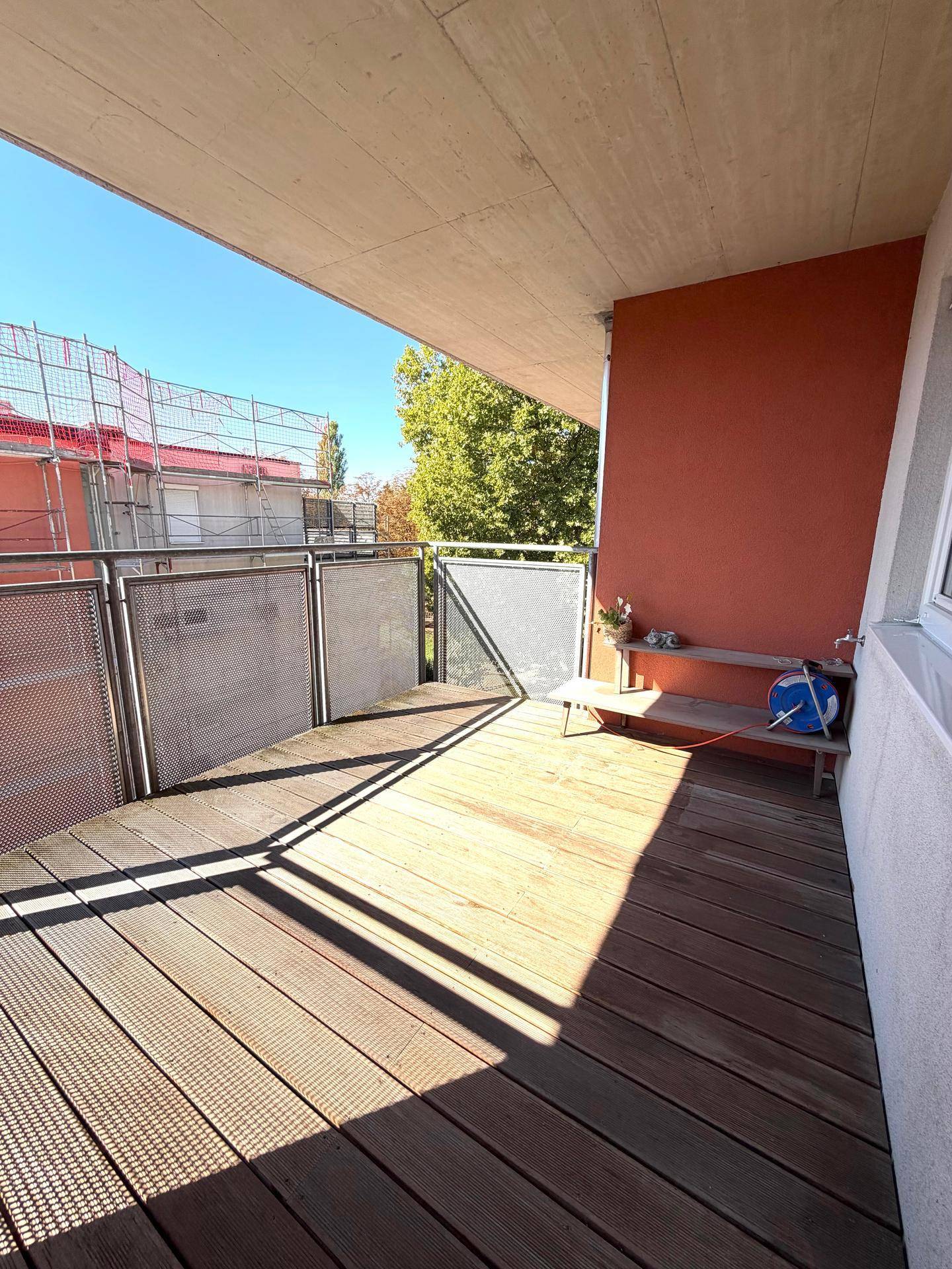 Sonniger Balkon mit Holzdeck und Metallgeländer, bietet einen Blick auf die Umgebung.