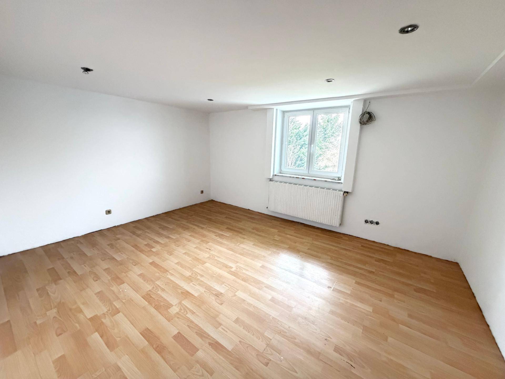 Helles Zimmer mit Holzboden, weißen Wänden und Einbaustrahlern in der Decke, viel Tageslicht.