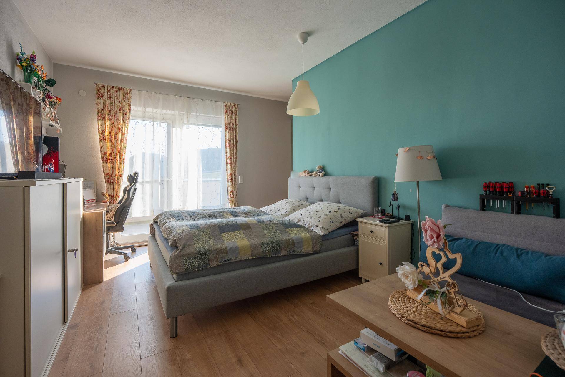 Helles Schlafzimmer mit Doppelbett, Holzfußboden und einem Schreibtisch am Fenster.