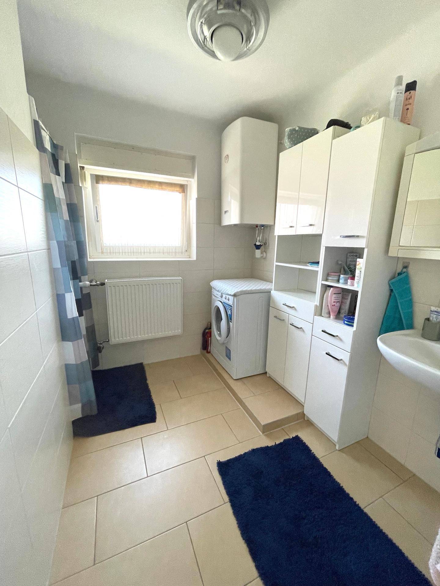 Geräumiges Badezimmer mit Duschkabine, Waschmaschine, Fenster und weißen Schränken.