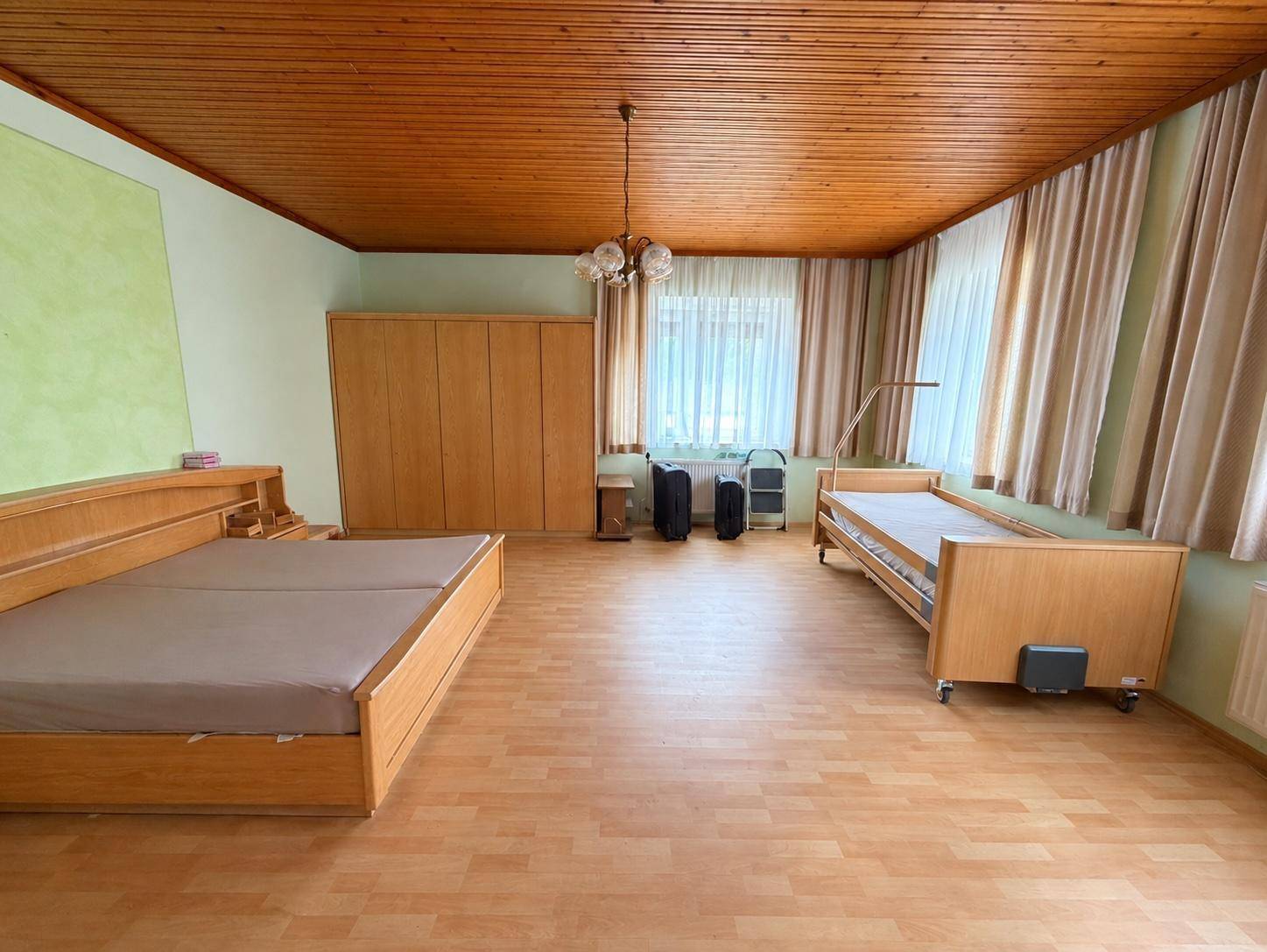 Großes Schlafzimmer mit zwei Betten, Holzdecke und Laminatboden.