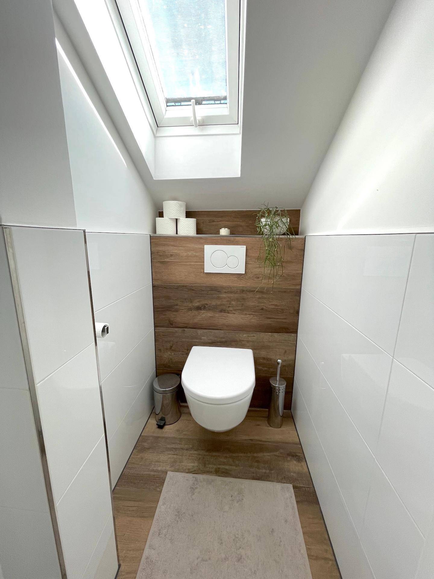 Modernes WC mit wandhängender Toilette, Holzverkleidung und einem Dachfenster für natürliches Licht.