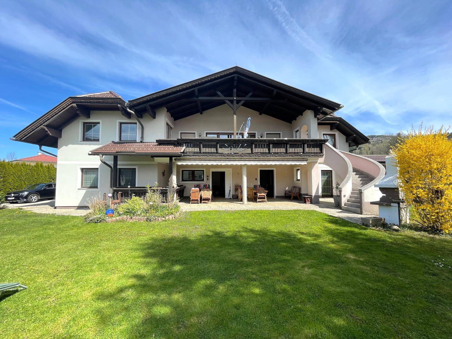 Die Rückseite des Hauses mit großem Garten, Balkon und Außentreppe unter blauem Himmel.