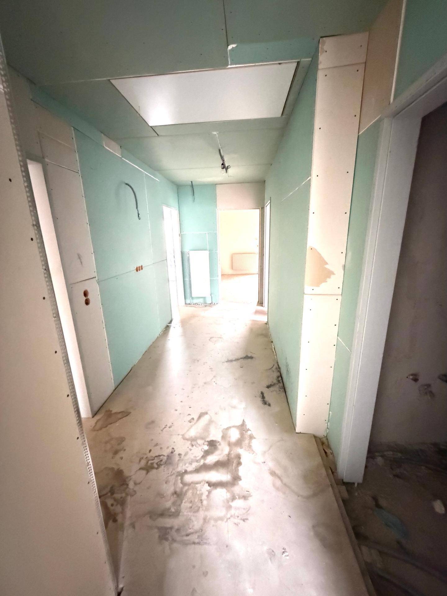 Flur im Rohbauzustand mit grünen Gipskartonwänden und unfertigem Boden, bereit für die Fertigstellung.