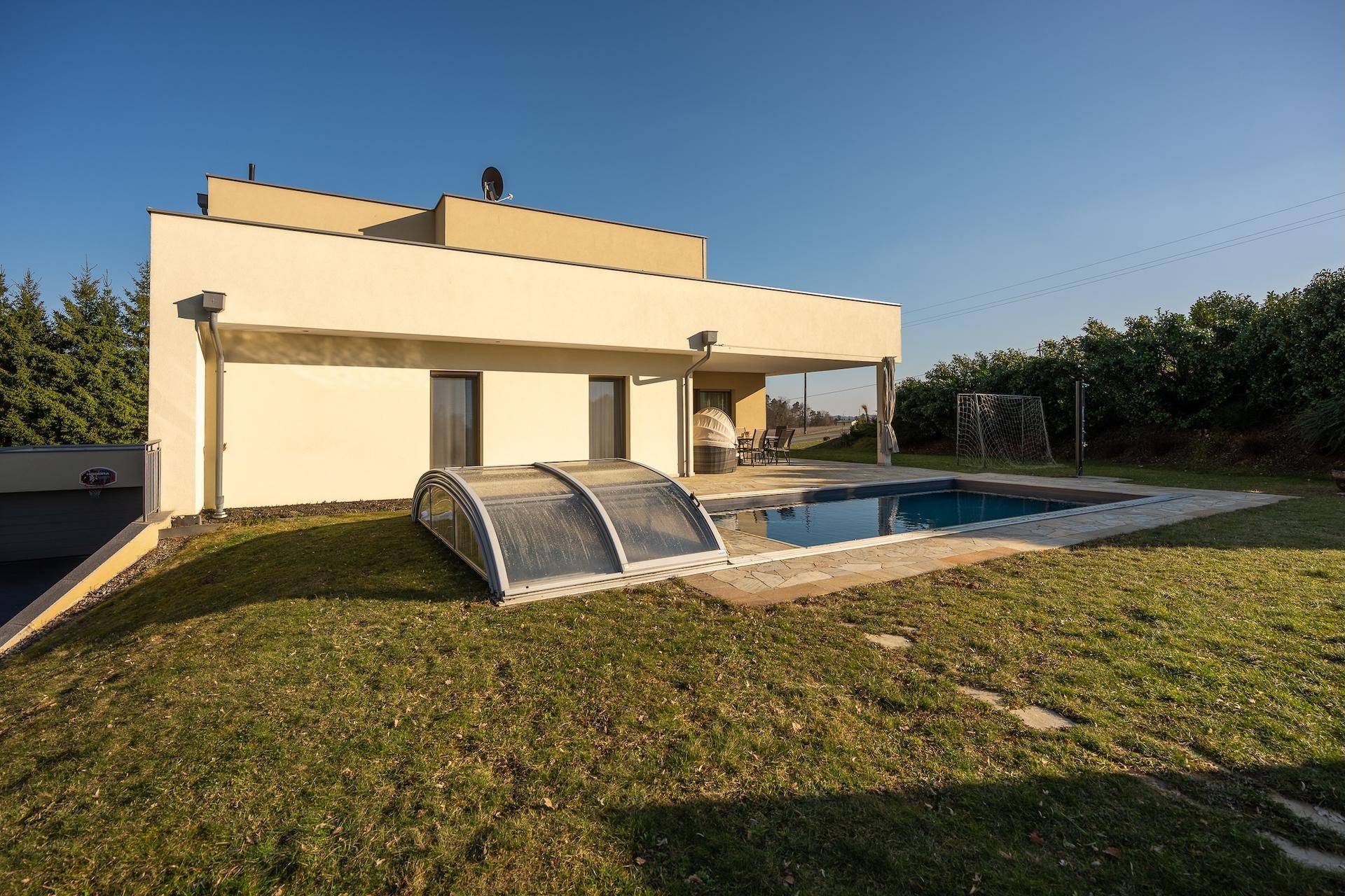 Modernes Haus mit Swimmingpool, großer Rasenfläche und überdachtem Terrassenbereich.