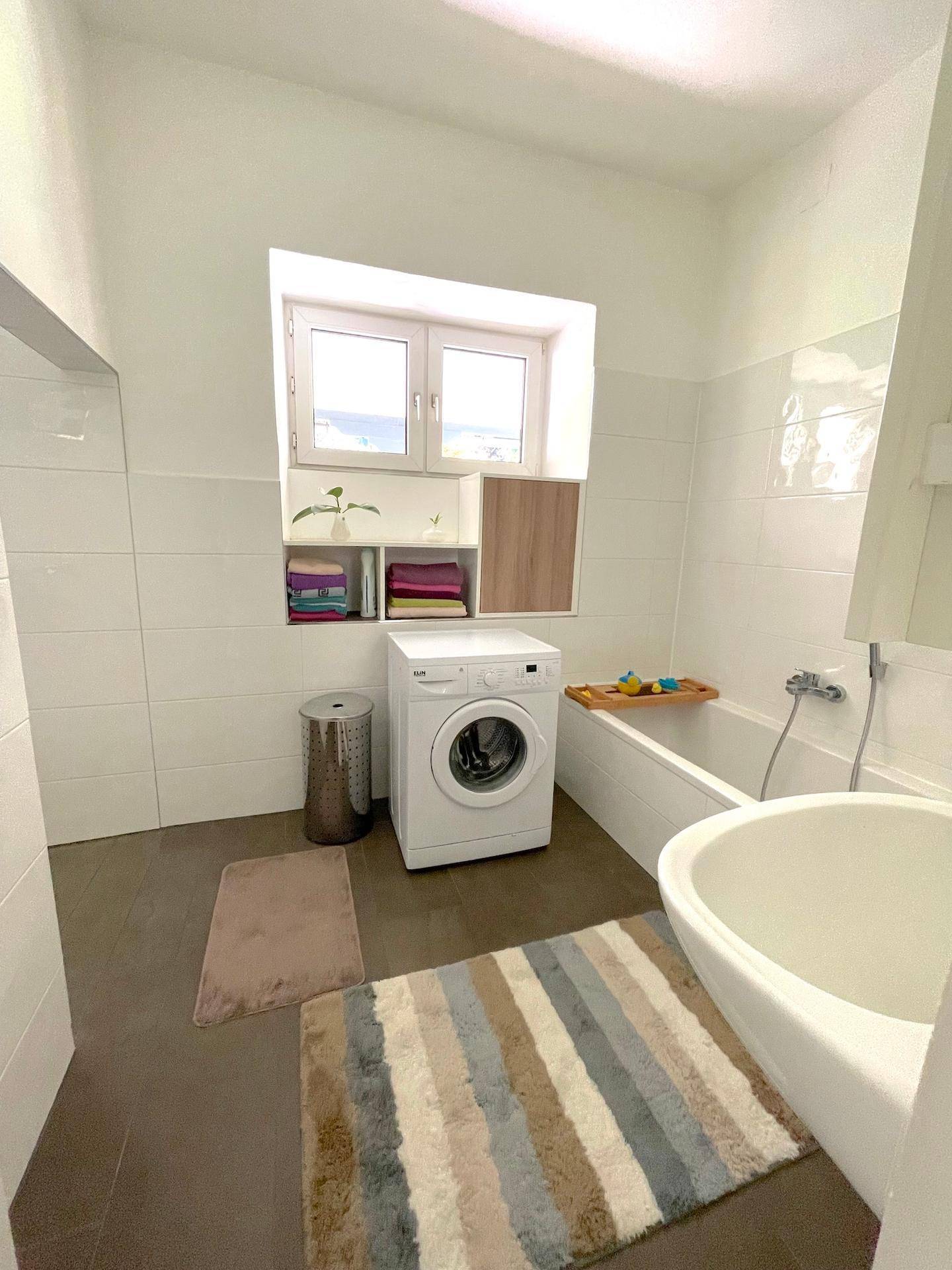 Helles Badezimmer mit Badewanne, Waschmaschine und Fenster, praktisch und funktional gestaltet.