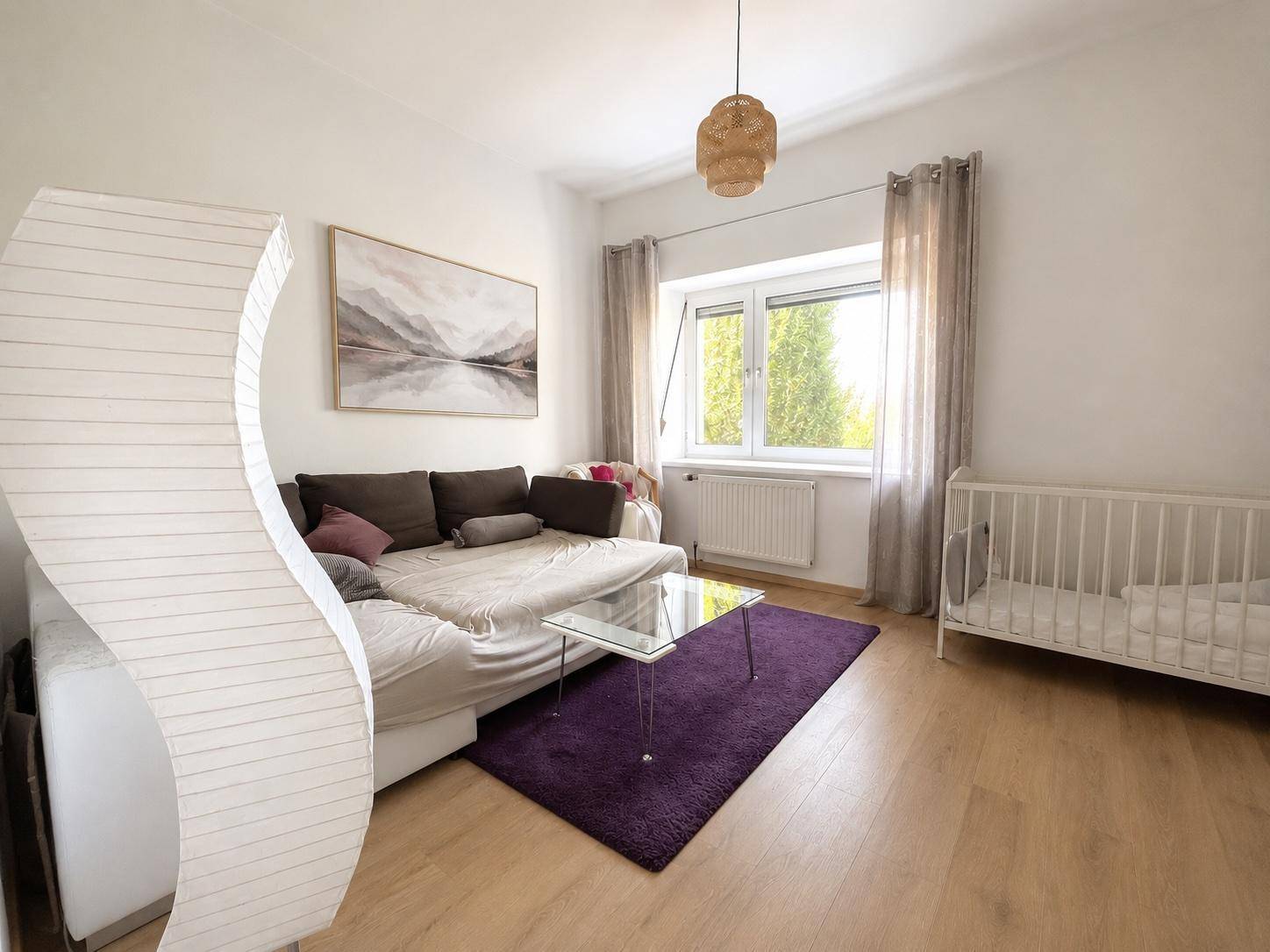 Helles Schlafzimmer mit Holzboden, gemütlichem Sofa und Babybett, ideal für Familien.