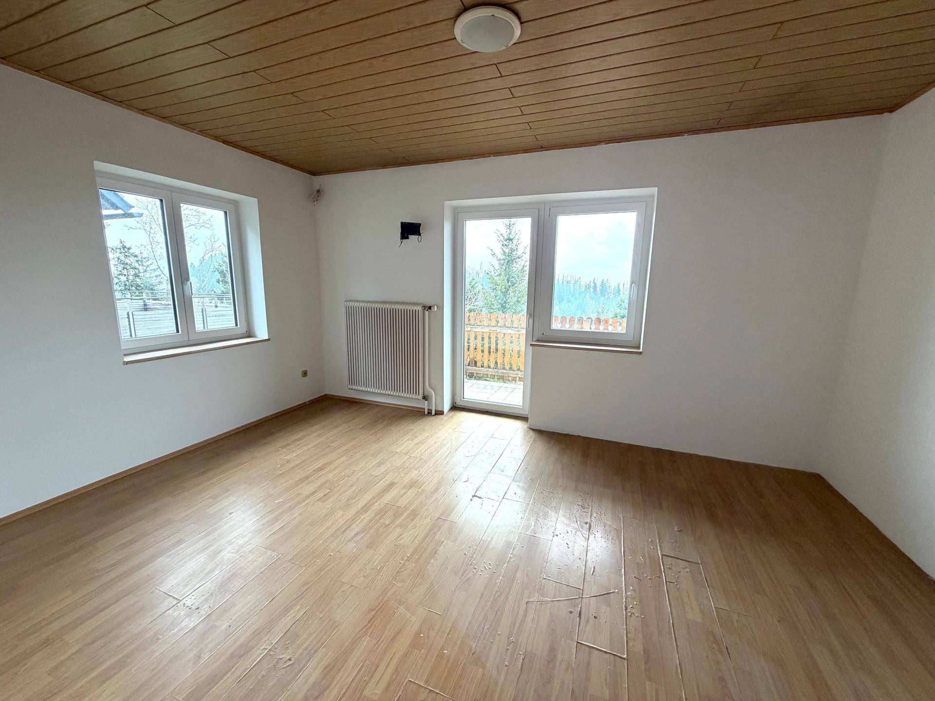 Helles Zimmer mit Holzdecke, Holzboden und Zugang zu einem kleinen Balkon mit Blick ins Grüne.