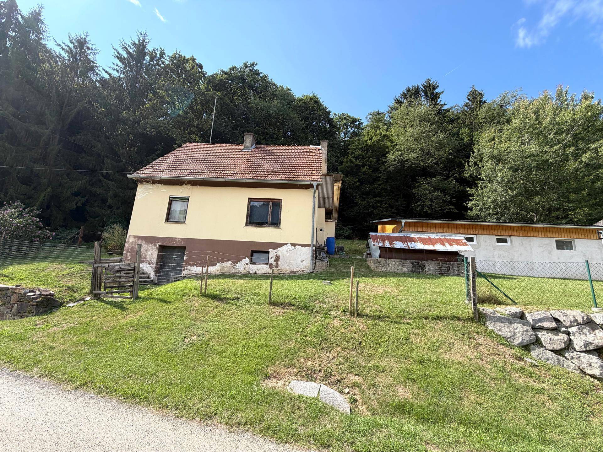 Rückseite eines älteren Hauses mit Nebengebäude und umzäuntem Gartenbereich in ländlicher Lage.