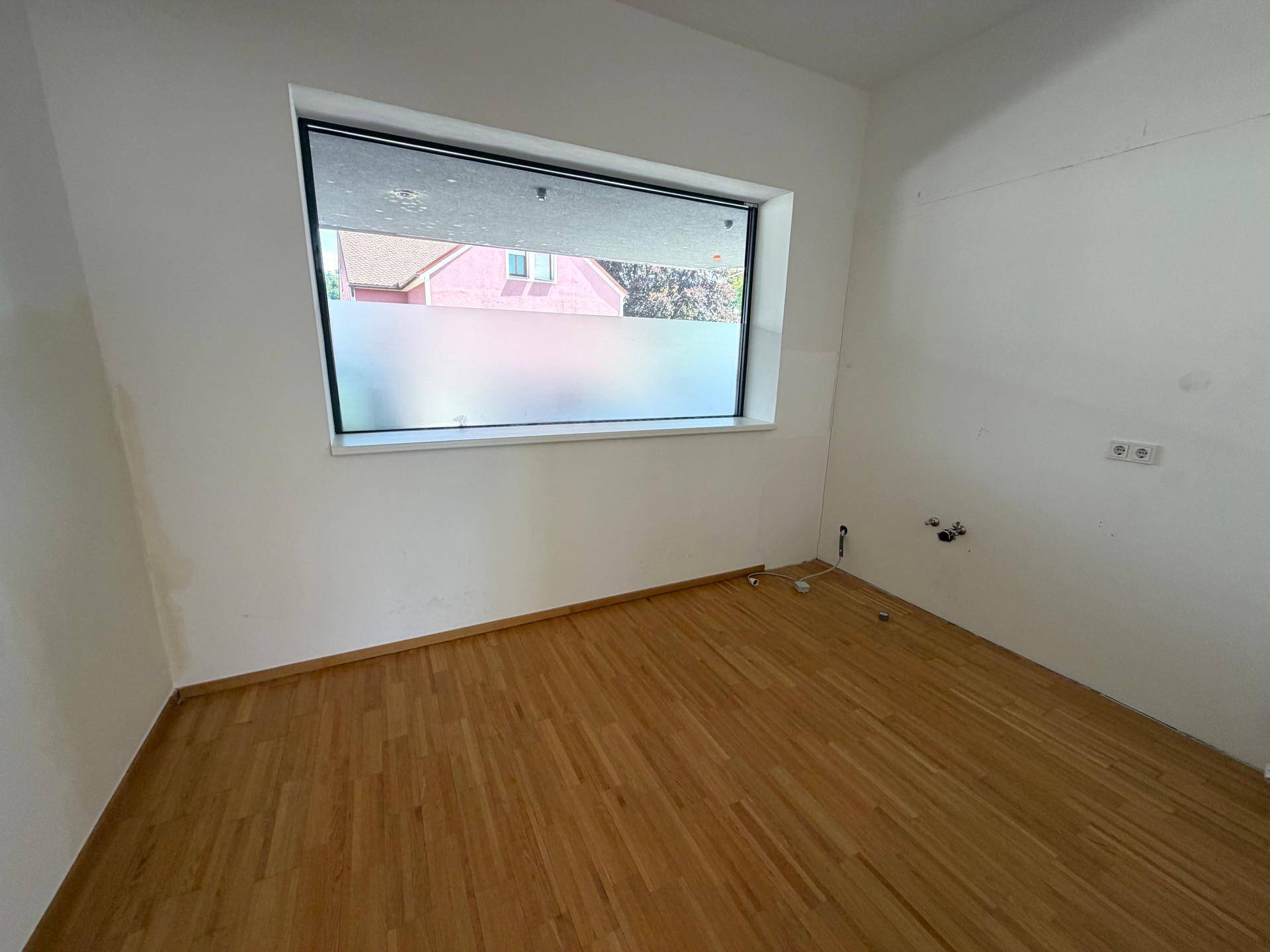 Leerer Raum mit Holzfußboden, weißen Wänden und einem Fenster mit Sichtschutzfolie.
