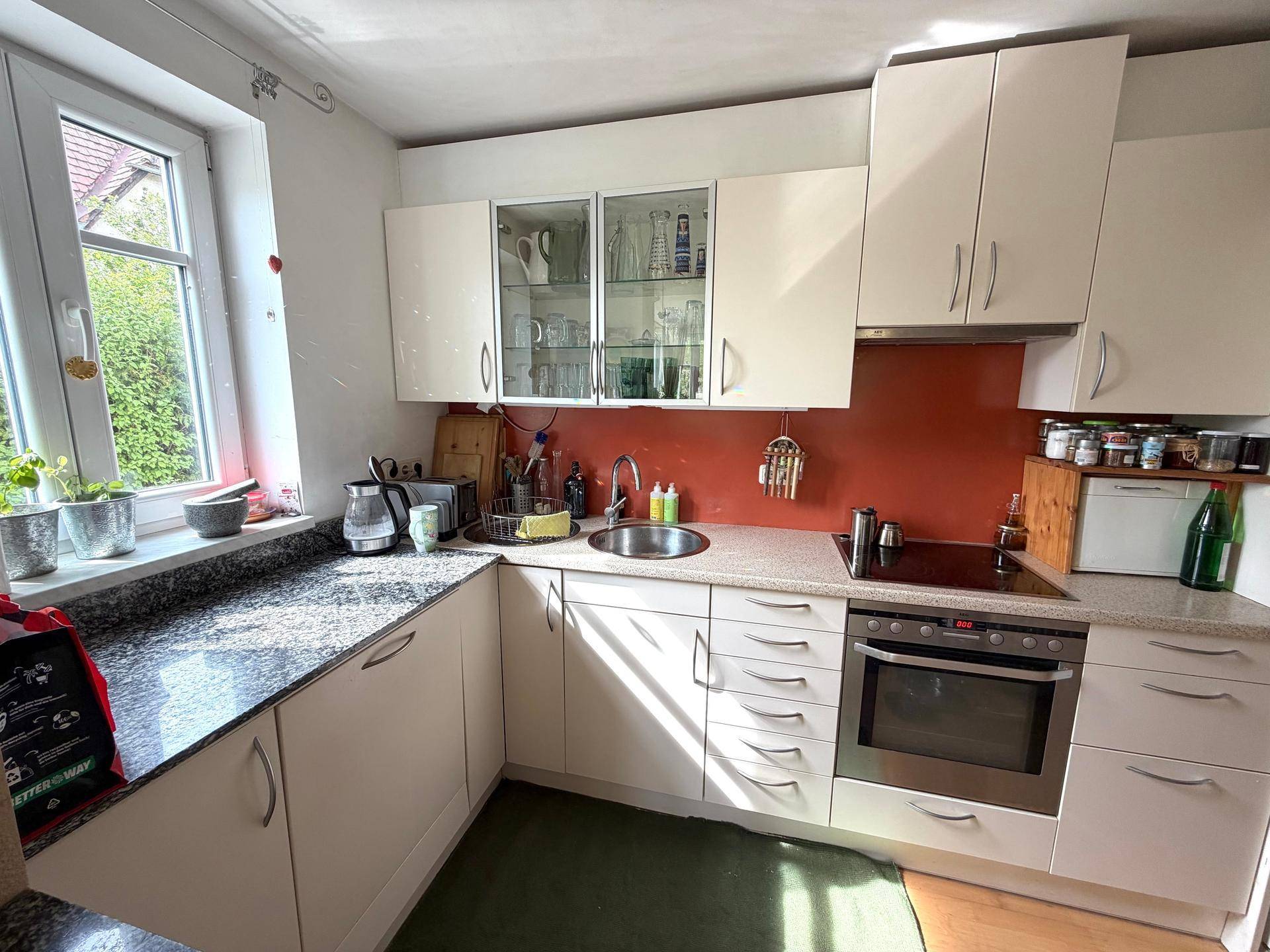 Funktionale Küche mit hellen Schränken, Granitarbeitsplatte und Fenster mit Blick ins Grüne.