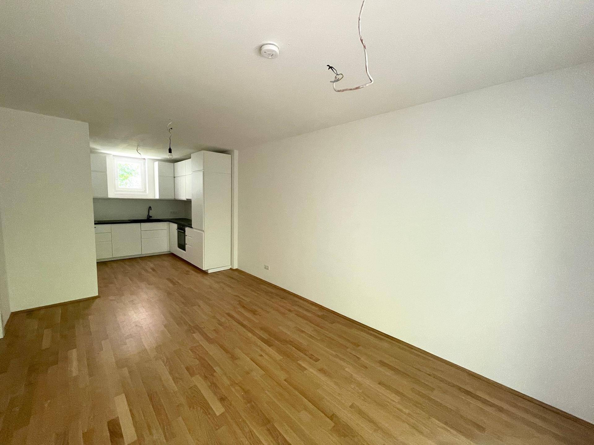 Heller, offener Wohnbereich mit Holzboden und Blick auf die moderne Einbauküche im Hintergrund.