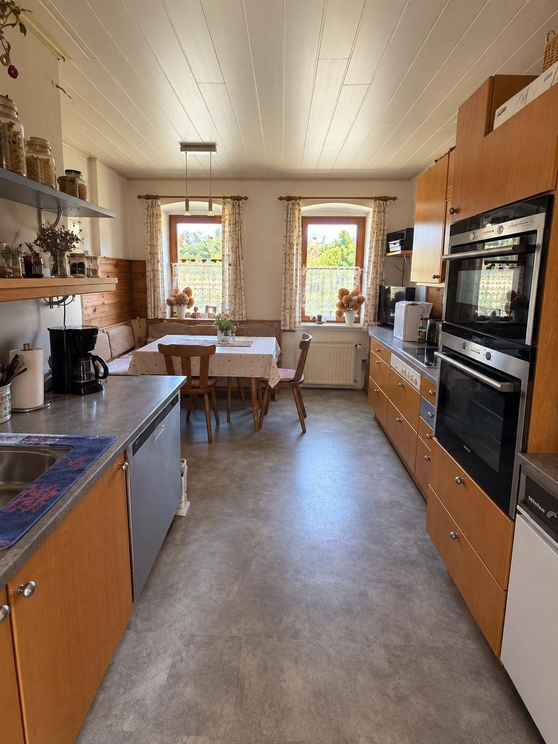 Gemütliche Küche mit Holzeinbauten, Essbereich und Blick ins Grüne durch zwei Fenster.