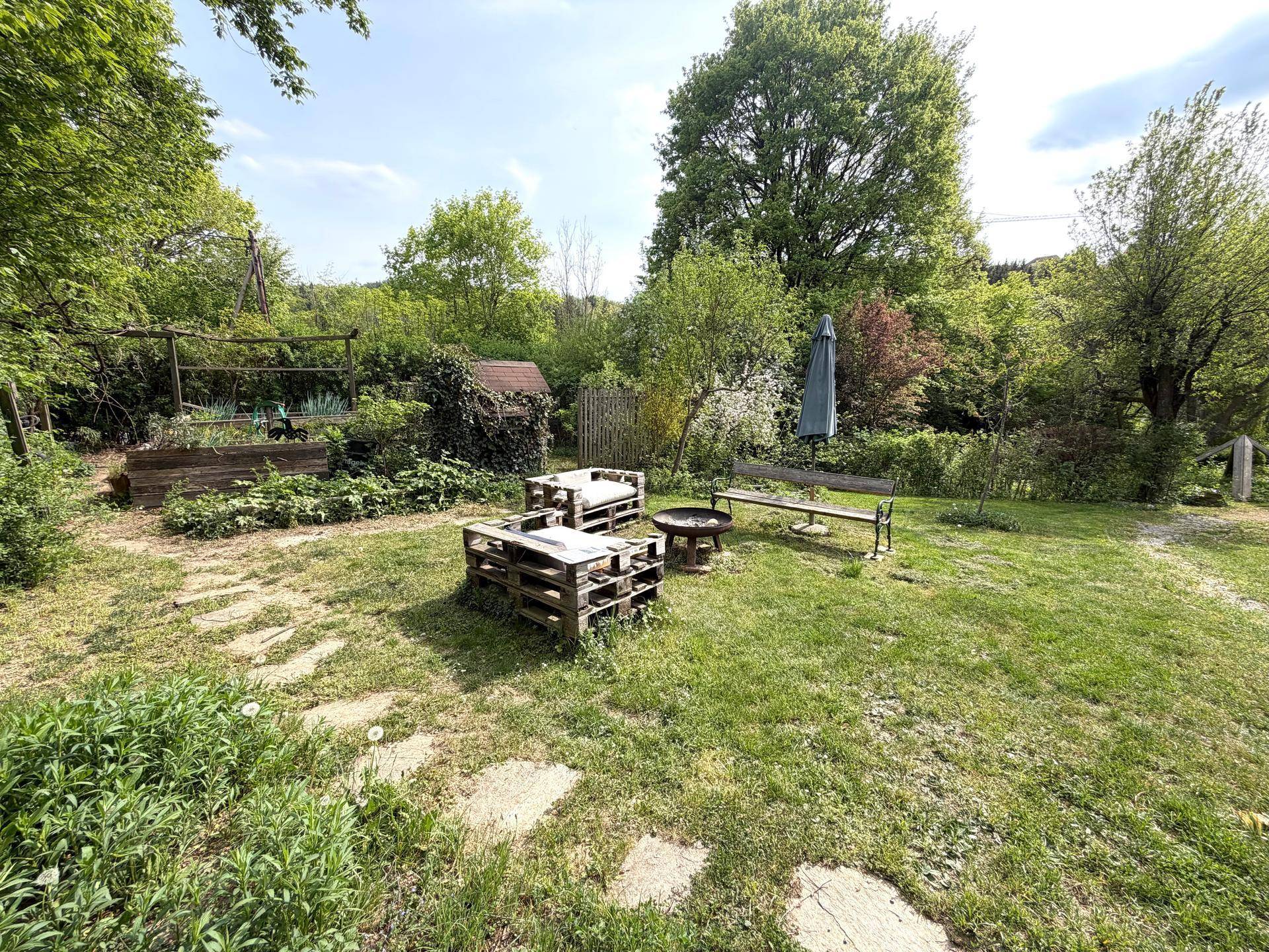 Gemütlicher Gartenbereich mit Palettenmöbeln, Feuerstelle und viel Grün zum Entspannen im Freien.