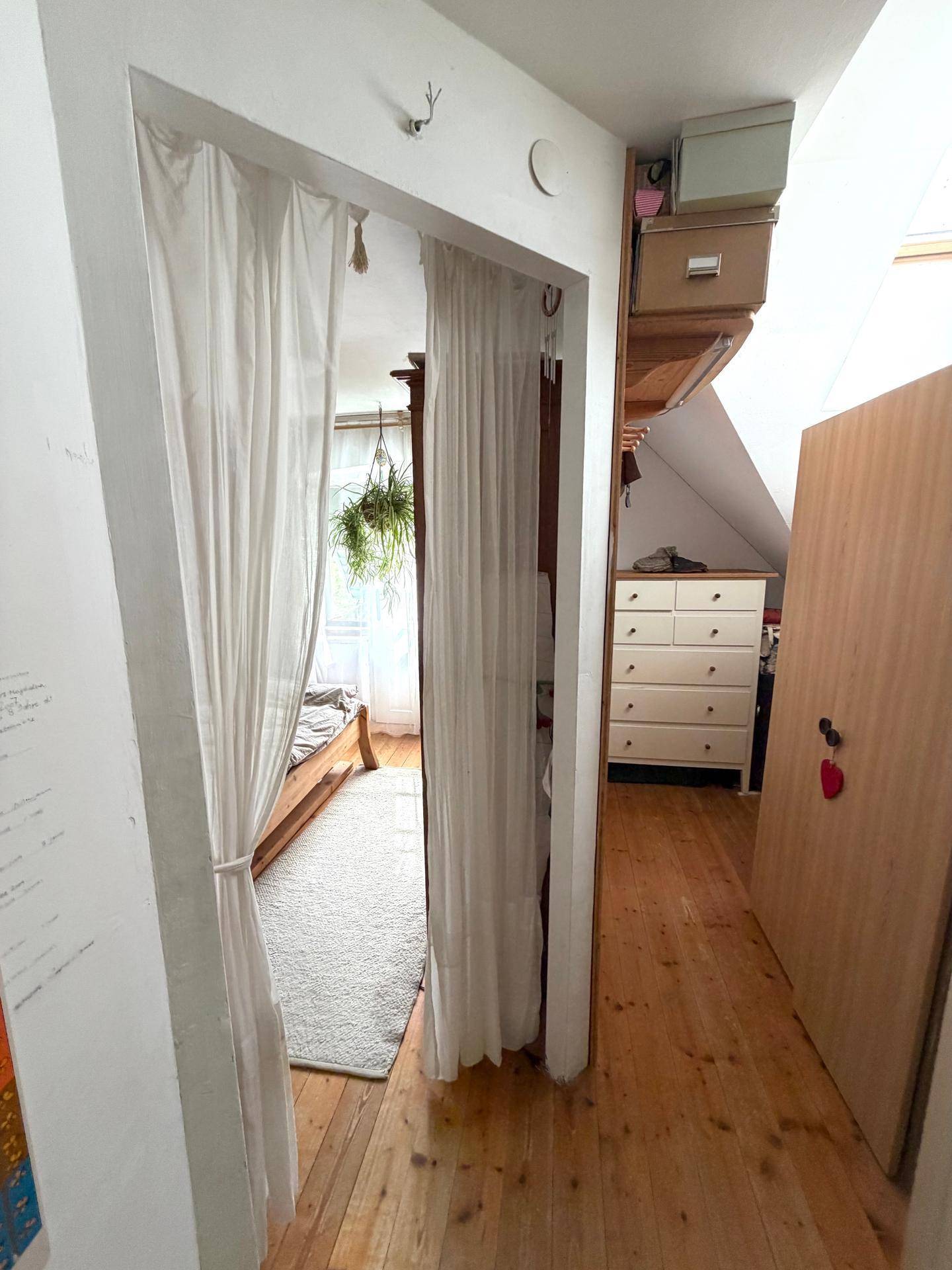 Heller Flur mit Holzboden und Zugang zu einem Schlafzimmer im Dachgeschoss.