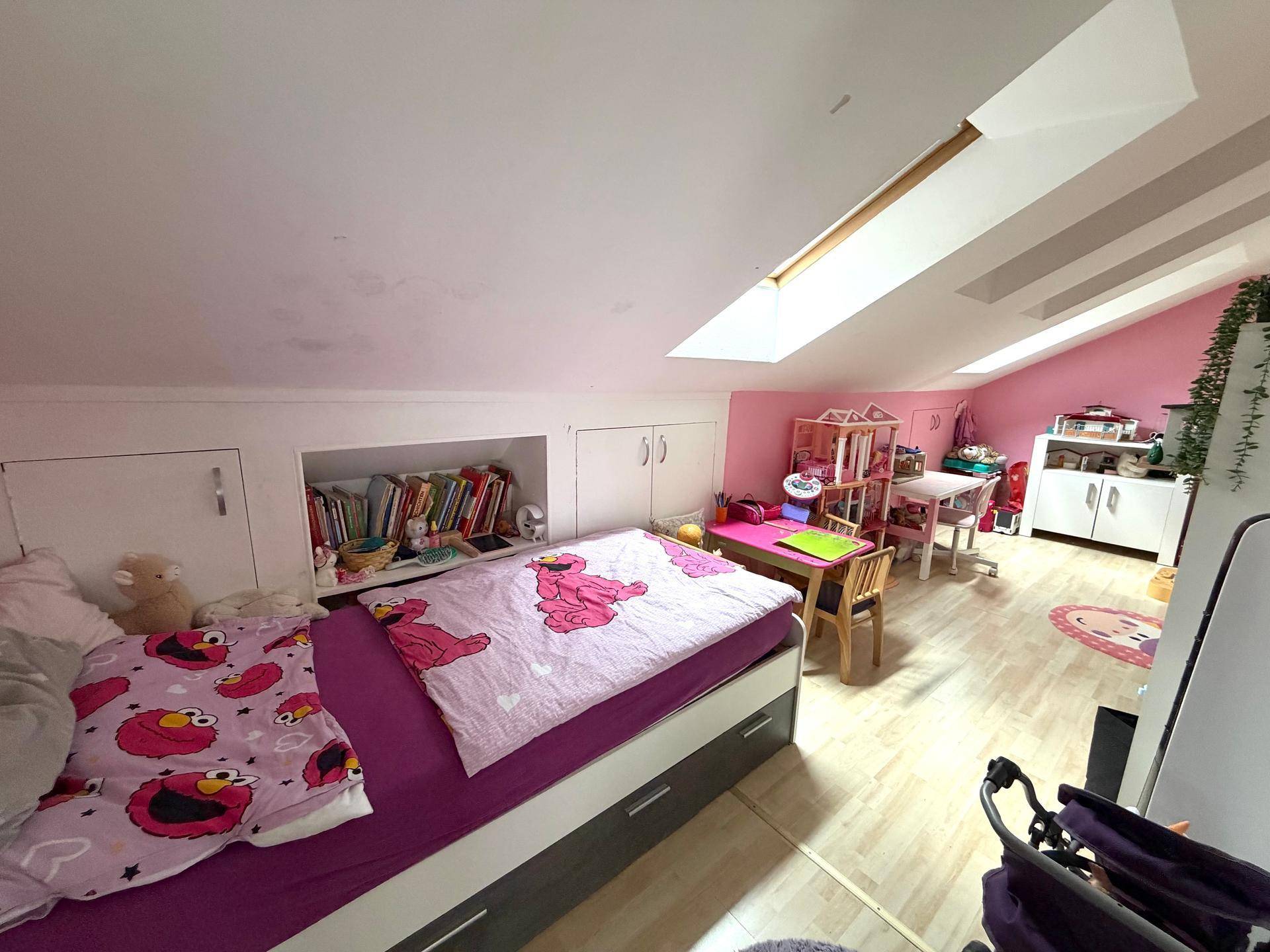 Geräumiges Kinderzimmer im Dachgeschoss mit Bett, Spielzeug und Dachfenstern, rosa Akzentwände.